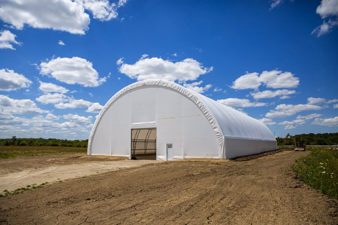 White engineered fabric riding arena building with an arched cover reaching to ground level, in a rural setting