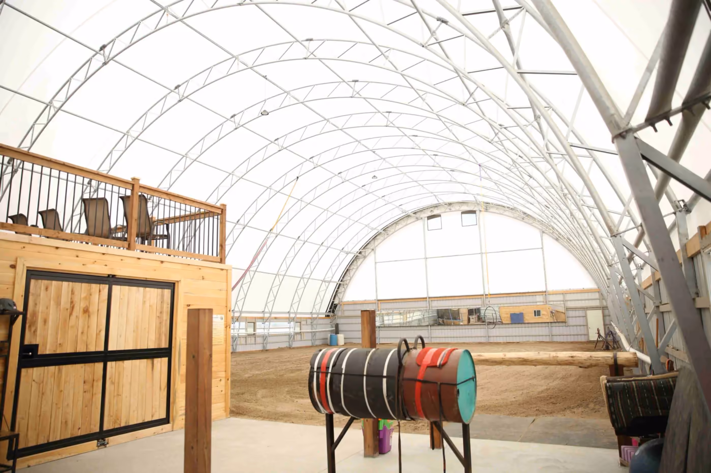 Interior of an engineered fabric riding arena on galvanised steel legs, with the truss frame visible and no internal columns across the riding surface