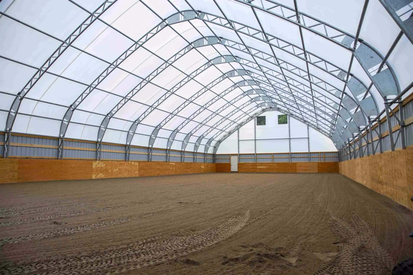 Interior of an engineered fabric riding arena with the truss frame carried on timber post side walls and a translucent cover