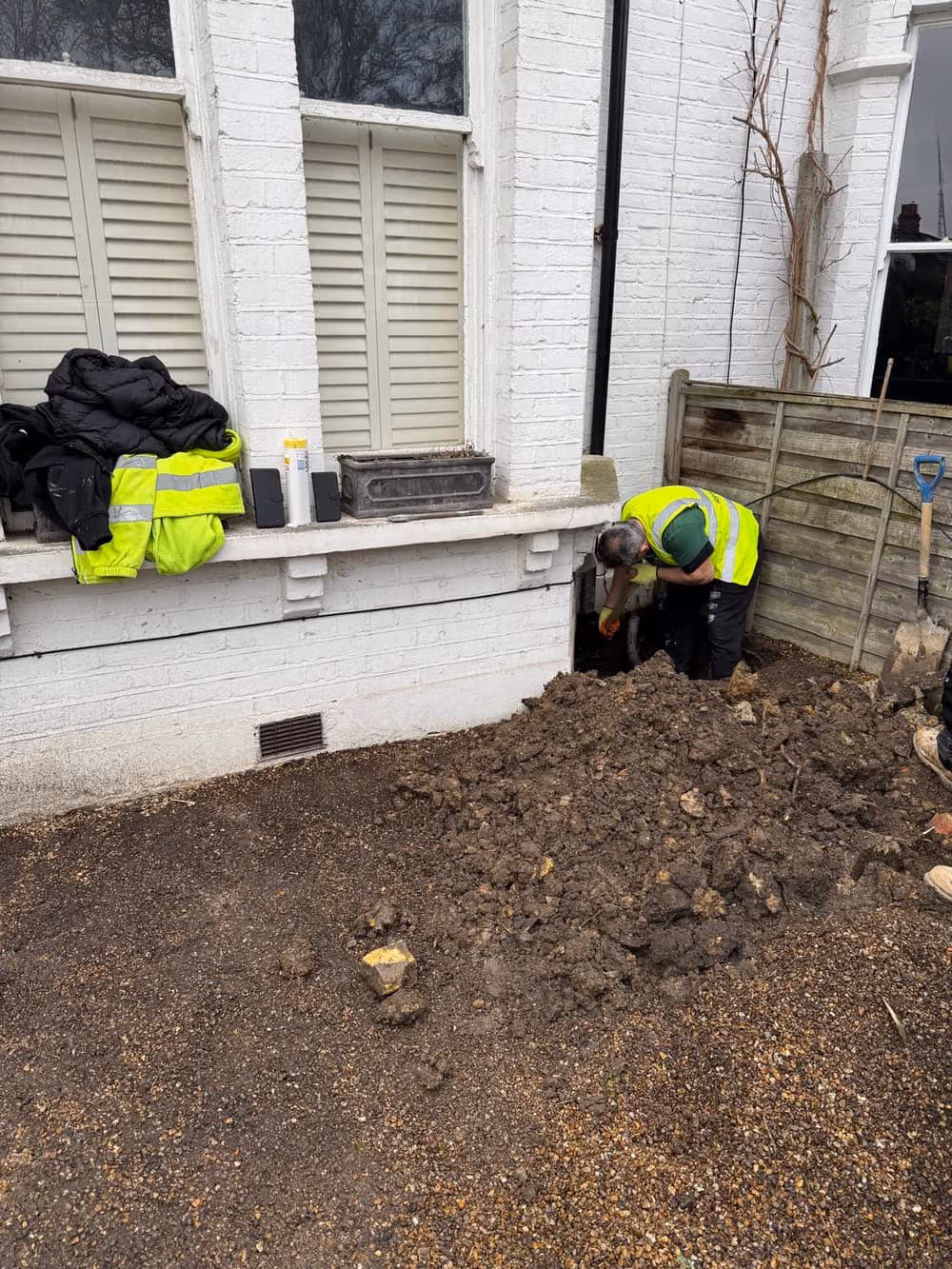 EMA site team excavating a trial pit at the base of a wall to expose the foundation for inspection, London