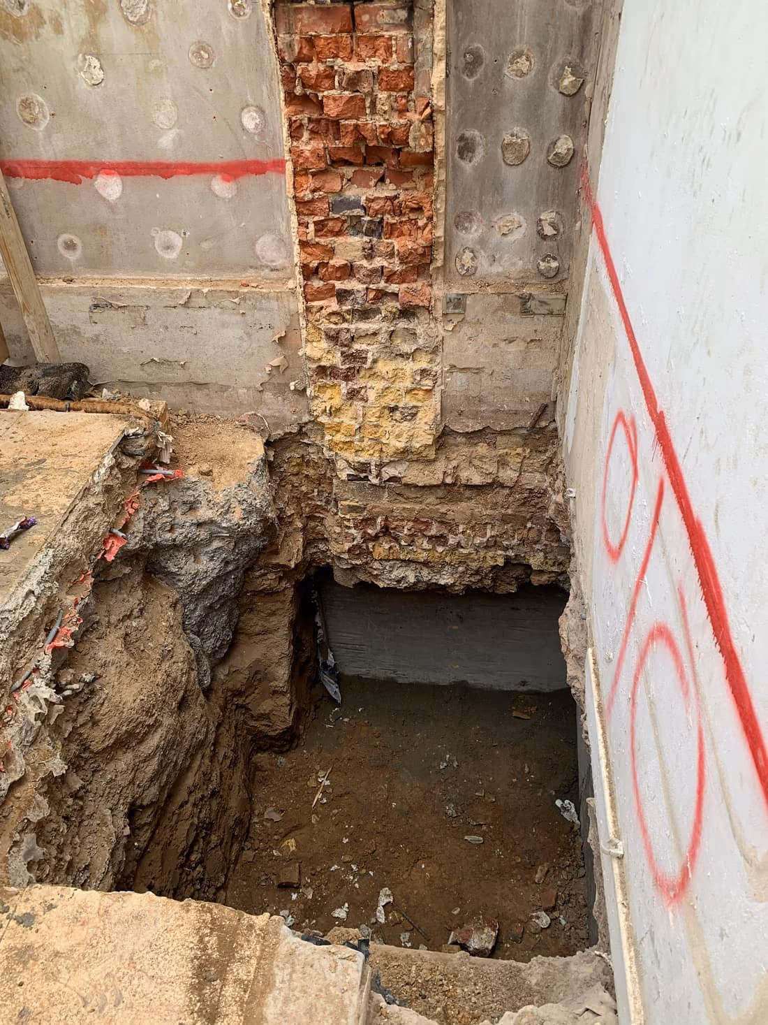 Mass concrete underpinning bay excavated in a hit-and-miss sequence beneath a wall in London, with survey markings